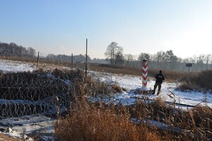  Funkcjonariusz SG stojący przy znaku granicznym przy polsko - białoruskiej granicy, w tle zaśnieżony krajobraz