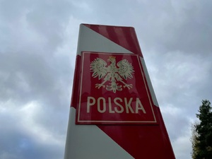 Znak graniczny Polska Znak graniczny z godłem i napisem Polska na tle pochmurnego nieba.