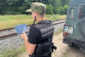 Funkcjonariusz SG Funkcjonariusz SG, stoi przy samochodzie służbowym obok torów kolejowych. Operuje dronem