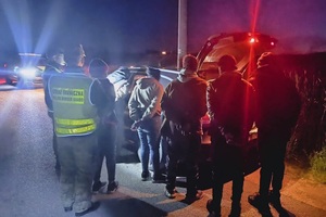 Zatrzymani migranci Dwóch funkcjonariuszy Straży Granicznej oraz kilku migrantów stoją tyłem, przed nimi pojazd osobowy. W tle pojazdu służbowy straży granicznej.