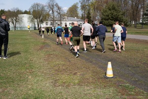 I Ty możesz zostać funkcjonariuszem Straży Granicznej Grupa osób w strojach sportowych biegnie po trawie wyznaczoną trasą oznaczoną pachołkami. Uczestnicy oddalają się a obok trasy stoi jedna osoba, która nadzoruje bieg. W tle widać budynek oraz drzewa.