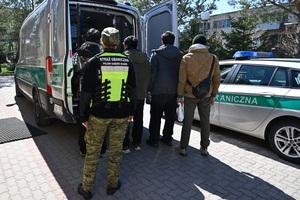 Z Litwy do Polski poza prawem Funkcjonariusz Straży Granicznej oraz czterech zatrzymanych mężczyzn stoi przy samochodzie.