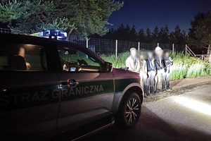 Weekendowe zdarzenia na granicy z Litwą zatrzymani stoją przy samochodzie służbowym straży granicznej